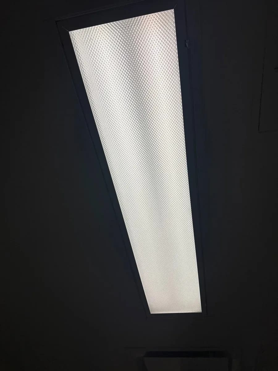 Rectangular illuminated ceiling light fixture with a textured diffuser in a dark ceiling.