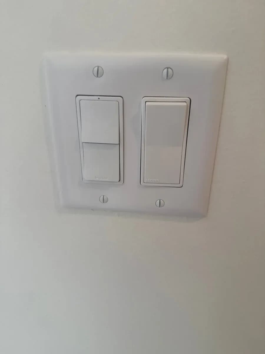 Completed installation of a white wall plate with two rocker light switches.
