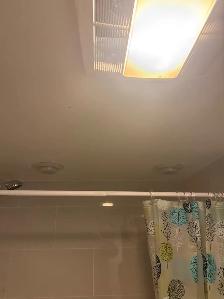 Illuminated rectangular ceiling light in a tiled bathroom above a shower curtain.