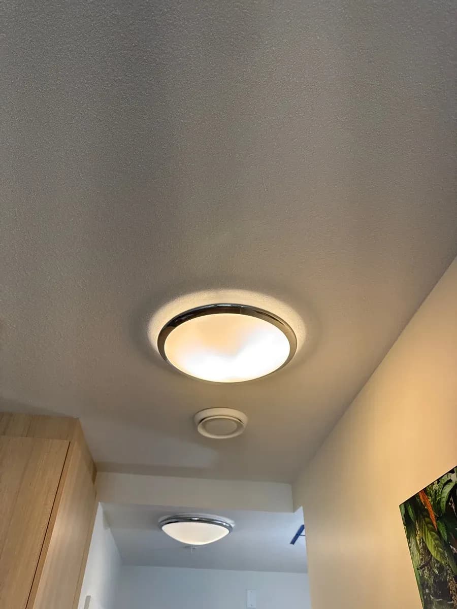 Interior ceiling with two illuminated flush-mount light fixtures and a smaller circular ceiling vent.