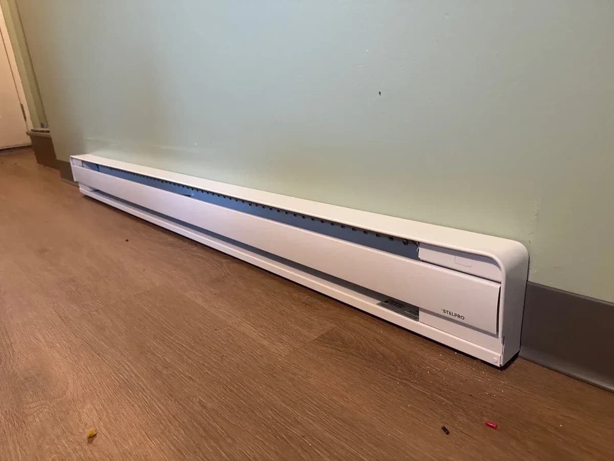 Completed wall-mounted electric baseboard heater installed along a light-colored wall above a wood-look floor.