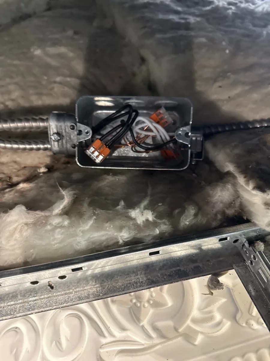 Open metal electrical junction box with black and white conductors joined by orange wire connectors and conduit entering from both sides.