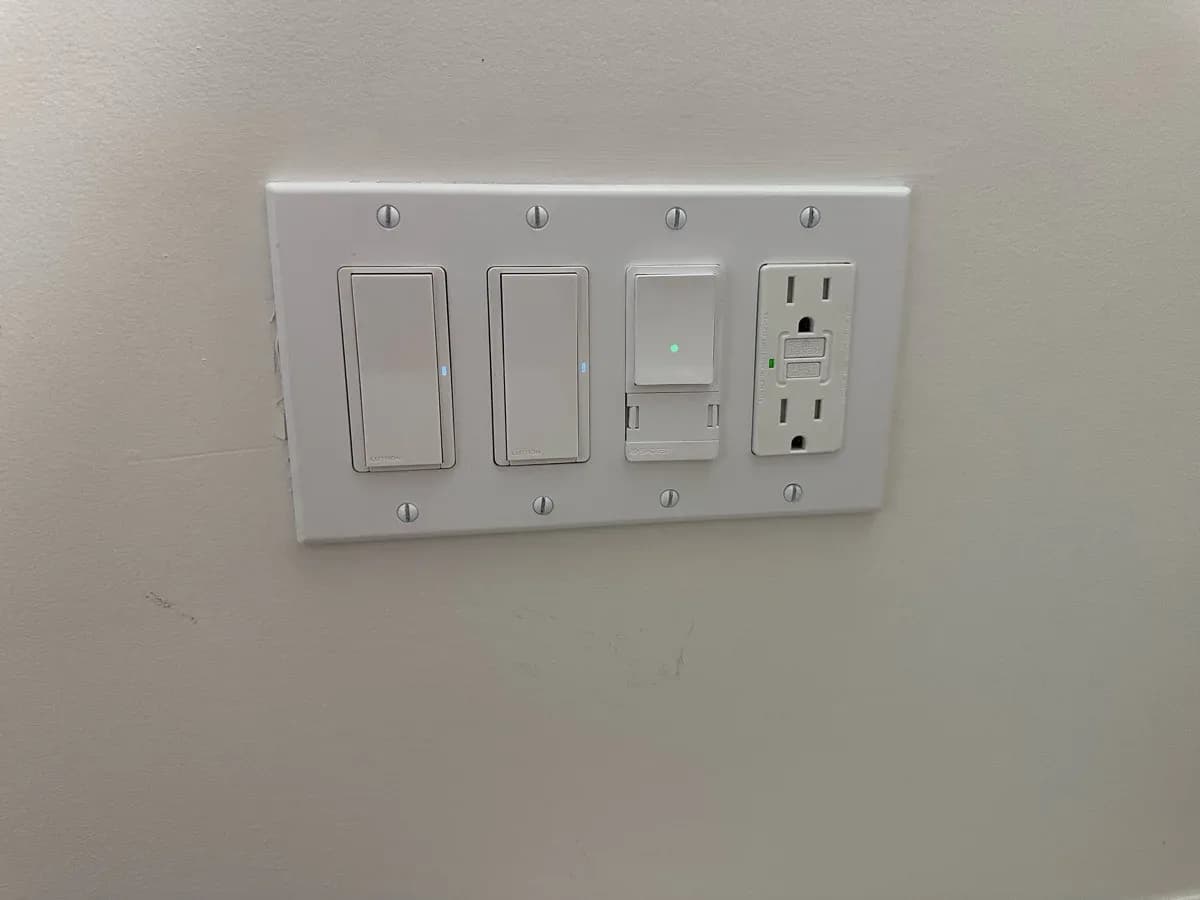 White wall plate containing two switches, a control with a green indicator light, and a GFCI receptacle.