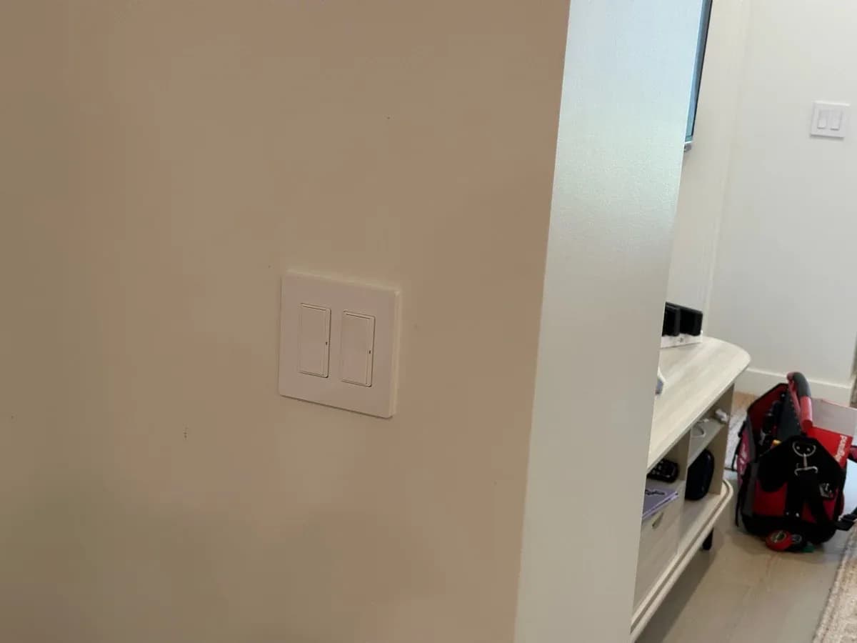 Wall-mounted white two-switch electrical plate installed on a light-colored interior wall.