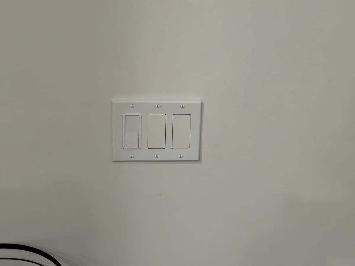 White three-switch electrical wall plate mounted on a light-colored wall.