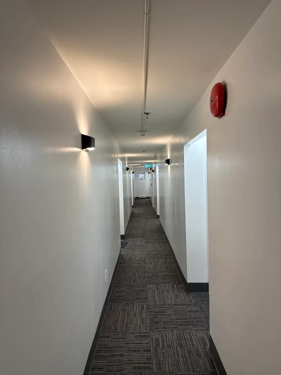 Completed hallway electrical installation with wall-mounted and ceiling lights, a red alarm device, and an illuminated exit sign.