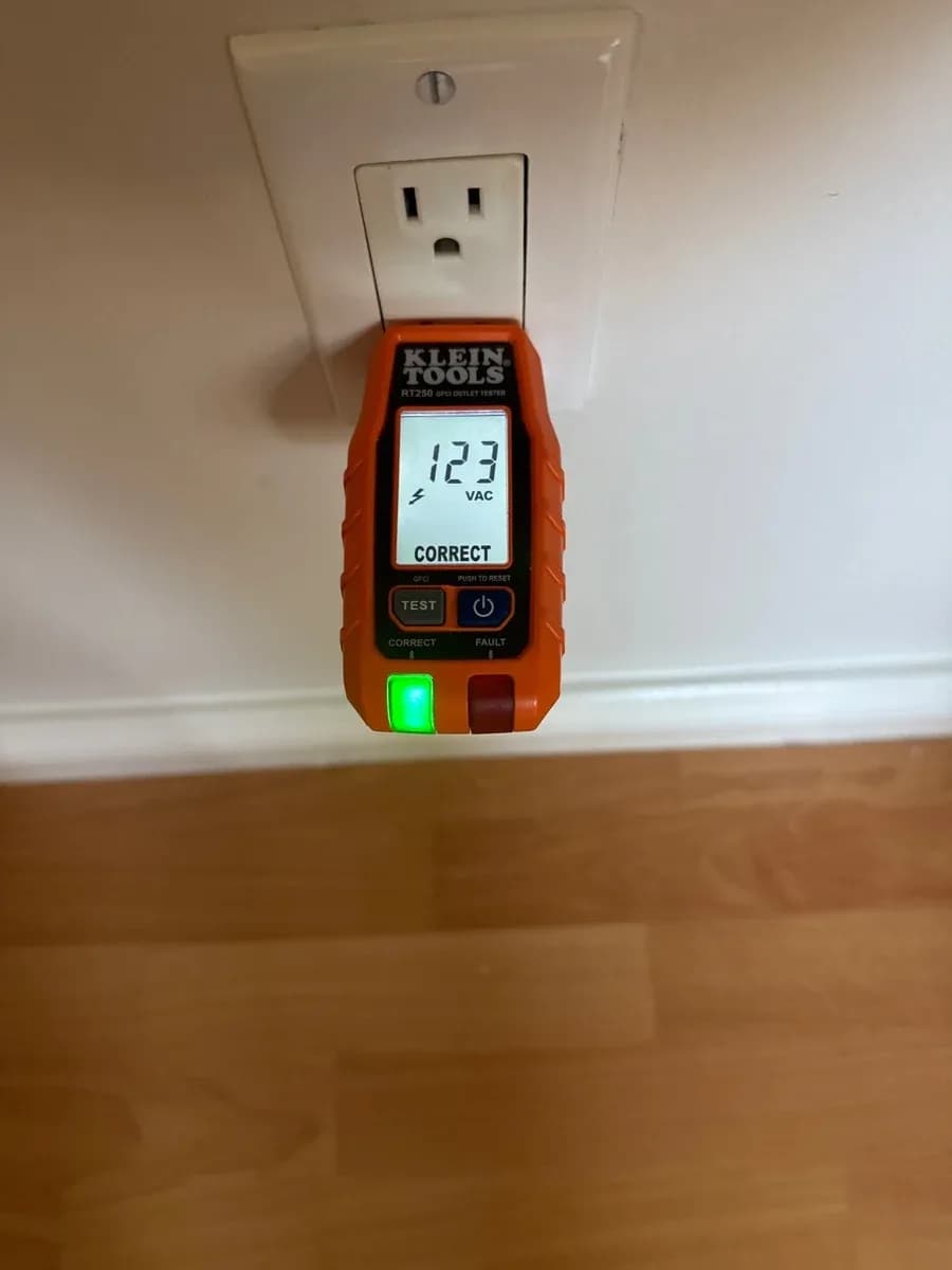 A plug-in electrical tester displays 123 VAC and indicates a correct receptacle connection at a wall outlet.