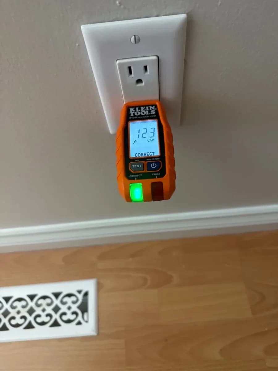 White wall receptacle with an orange plug-in tester displaying 123 VAC and a correct wiring indication.