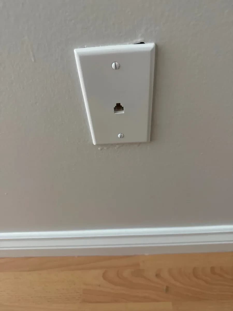 White wall plate with a single communication jack installed above a baseboard on a painted wall.