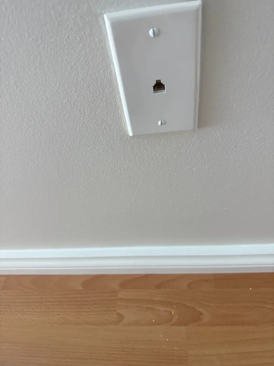 White wall plate with a single data jack installed above a baseboard and wood flooring.