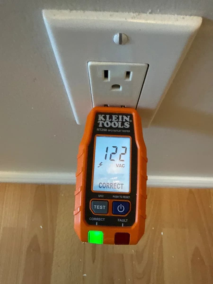 White electrical receptacle with a Klein Tools plug-in tester displaying 122 VAC and CORRECT.
