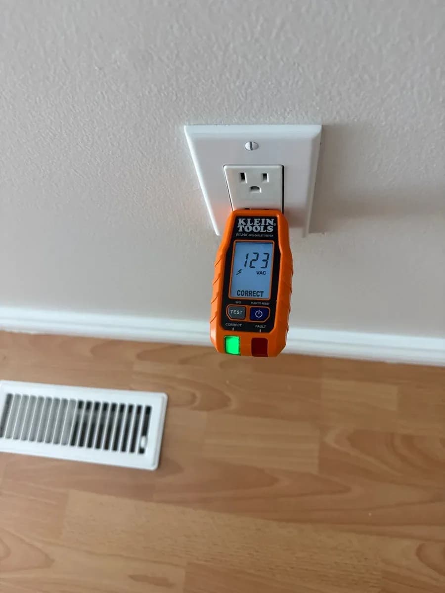 White duplex electrical receptacle with an orange plug-in tester displaying 123 VAC and a correct-wiring indicator.