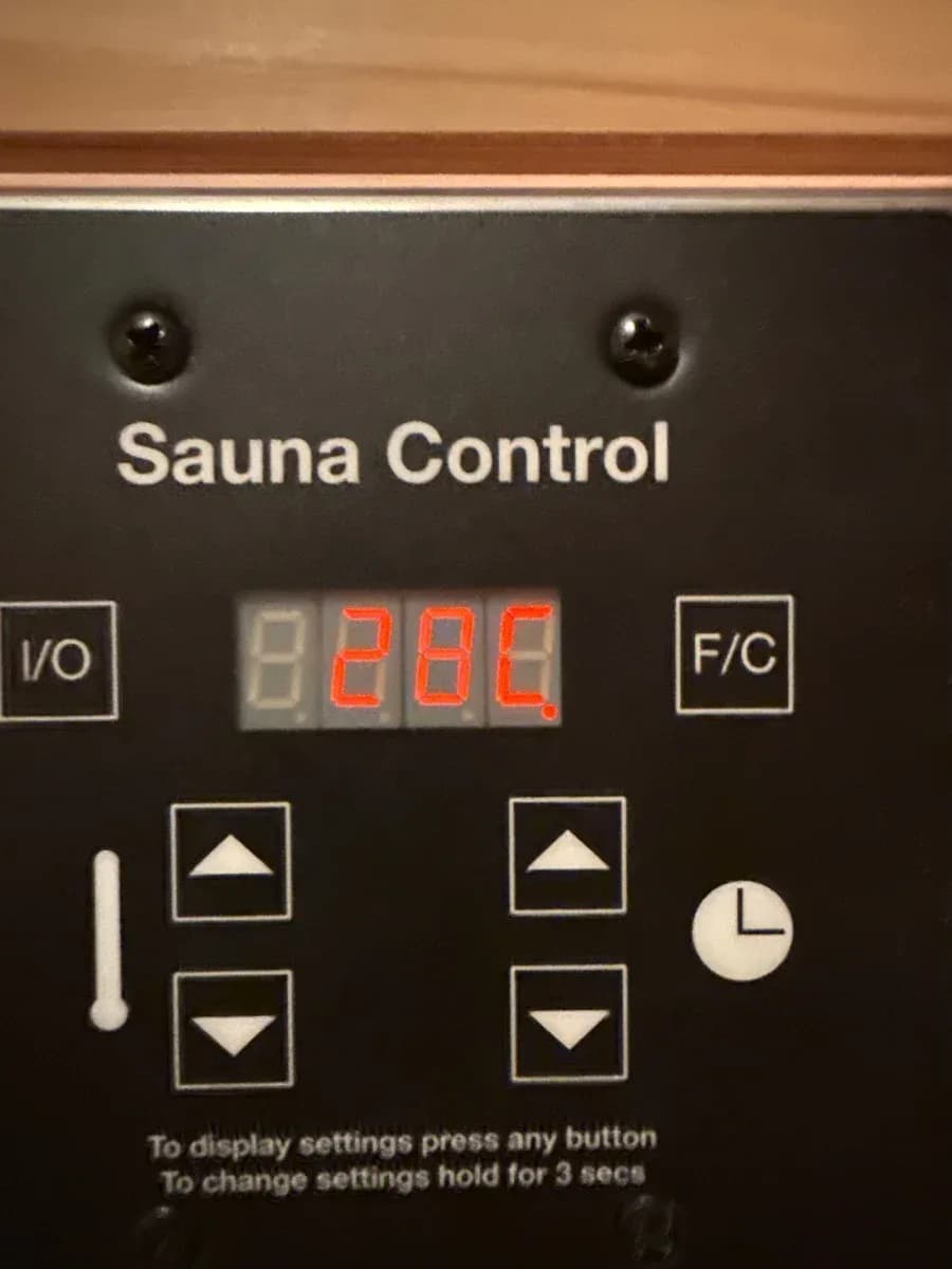 Close-up of a black sauna control panel labeled “Sauna Control,” showing a red digital temperature display, control buttons, and a clock icon.