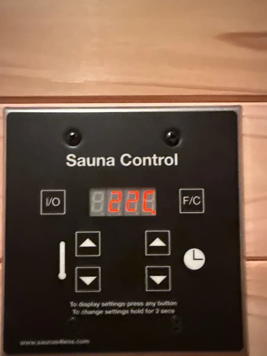Wall-mounted black sauna control panel displaying 22°C, installed on a wood-paneled wall.