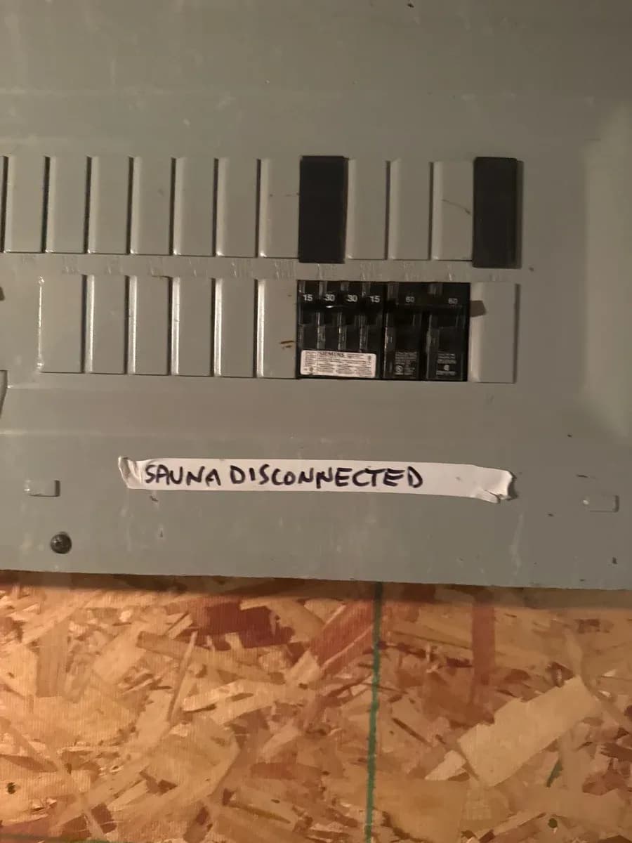 Electrical panel with multiple breakers and a handwritten label reading “SAUNA DISCONNECTED.”