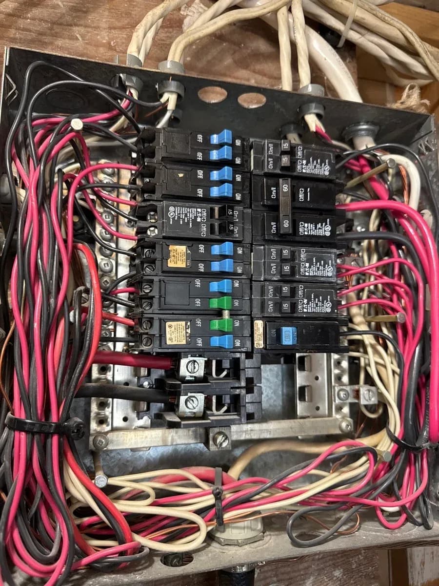 Open electrical service panel showing multiple circuit breakers, insulated conductors, and grounding hardware.