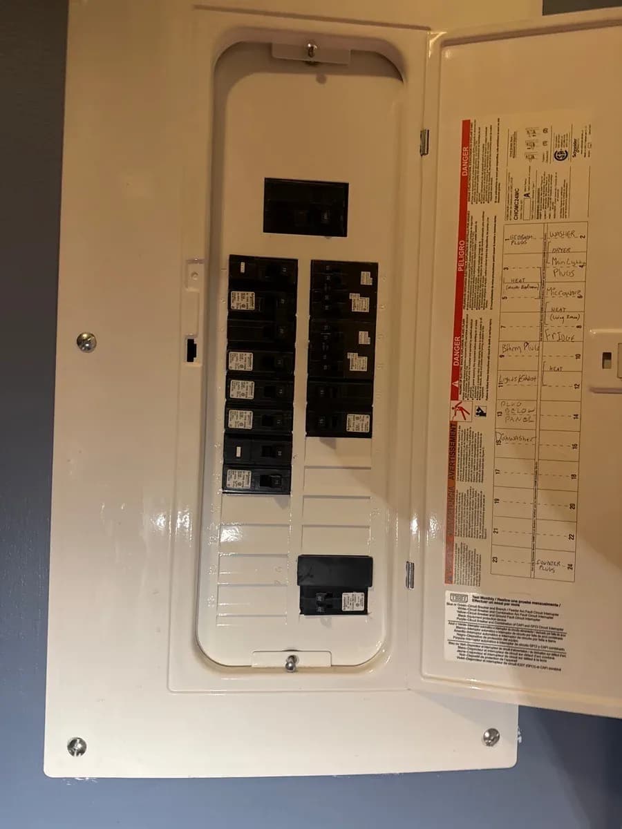 Open residential electrical panel showing installed circuit breakers, labeled circuits, and the panel door’s safety instructions.