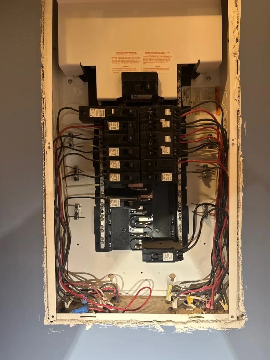 Open residential electrical service panel showing multiple circuit breakers and connected red, black, and white wiring.