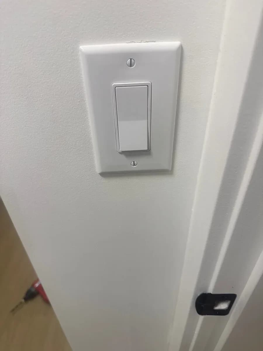 White wall-mounted rocker light switch with a matching rectangular cover plate beside a doorway.