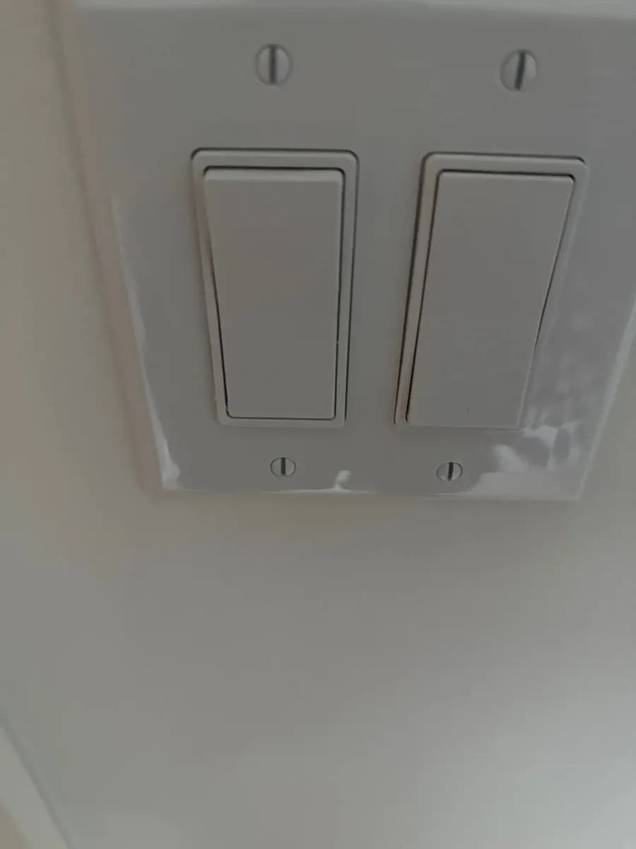 White wall plate with two side-by-side rocker light switches and visible mounting screws.