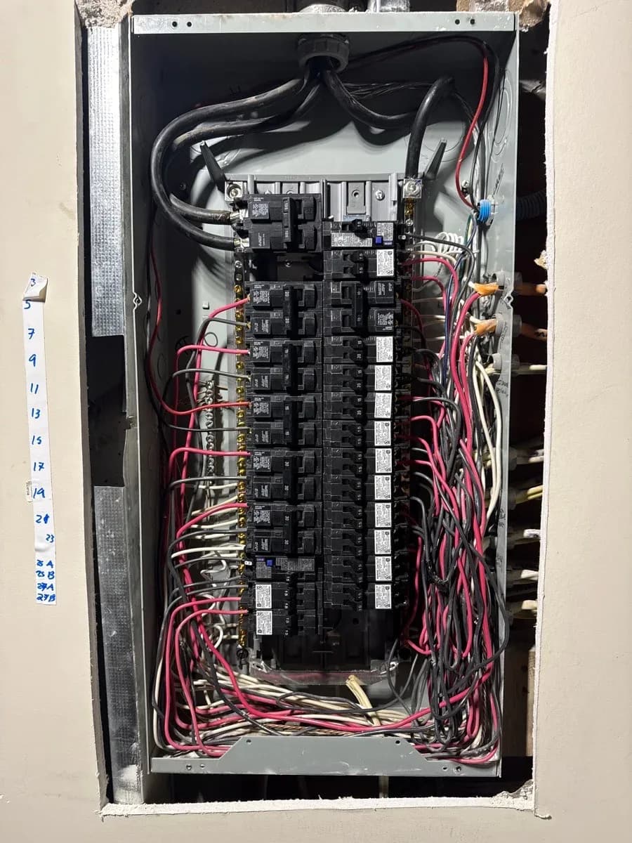 Open electrical distribution panel showing rows of circuit breakers and neatly routed black, red, and white conductors.