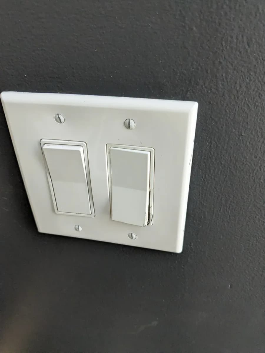 White two-switch electrical wall plate mounted on a dark textured wall.