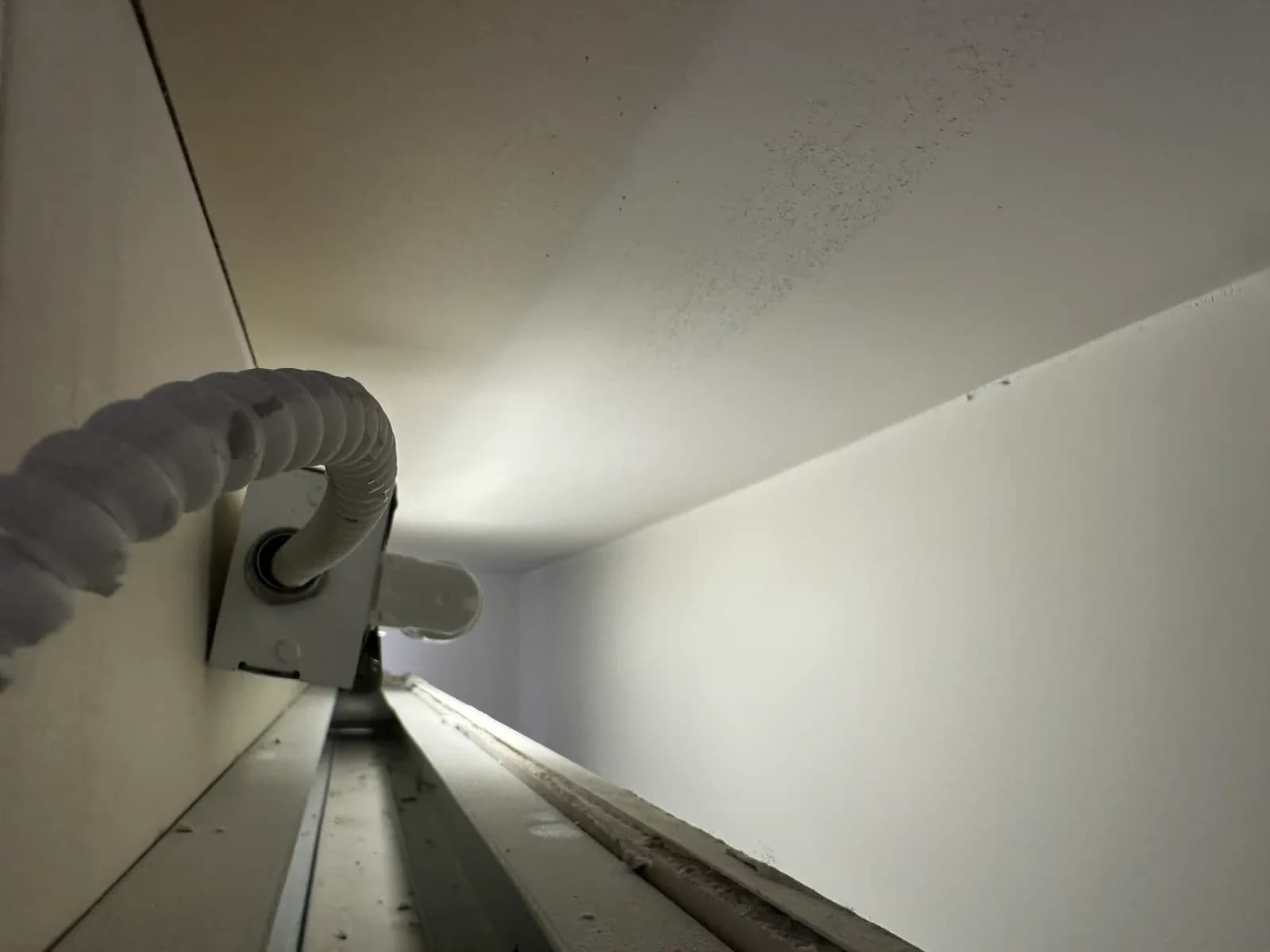 Close-up of flexible electrical conduit entering a mounted electrical box beside a long light fixture or channel.
