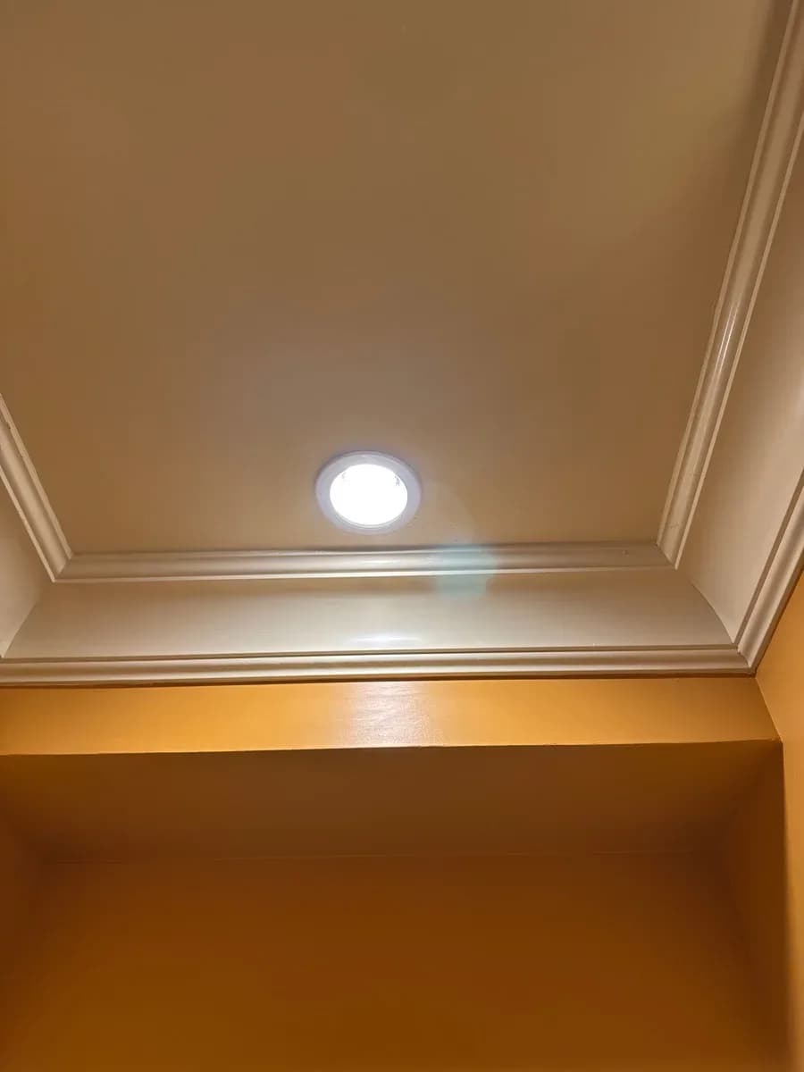 A bright recessed ceiling light installed in a finished tan ceiling with decorative trim.