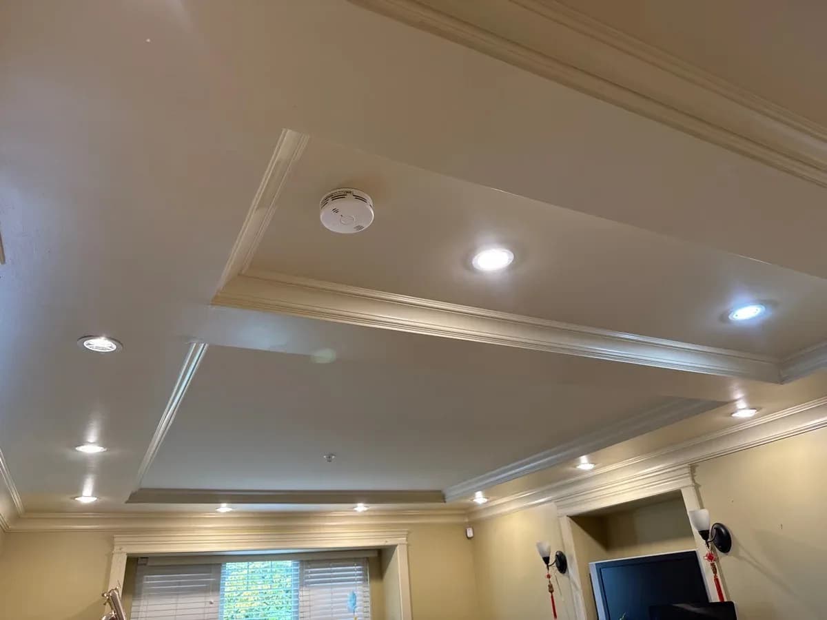Completed ceiling installation with multiple recessed lights and a smoke detector in a tray-ceiling room.