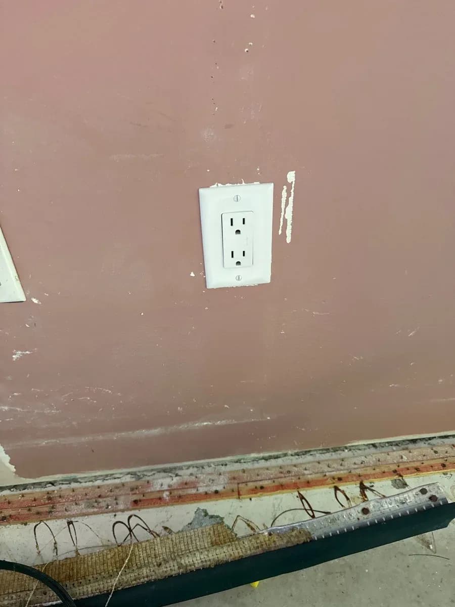 White duplex electrical receptacle installed on a painted wall above an unfinished floor edge.